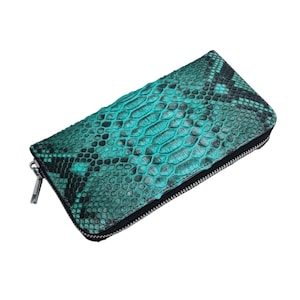 May include: A teal and black snakeskin-patterned wallet with a silver zipper. The wallet is rectangular and has a textured surface. The zipper pull is silver.