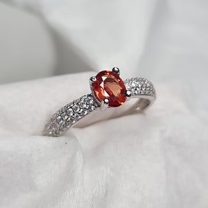 May include: A silver ring with a single oval-shaped orange gemstone surrounded by smaller white gemstones.