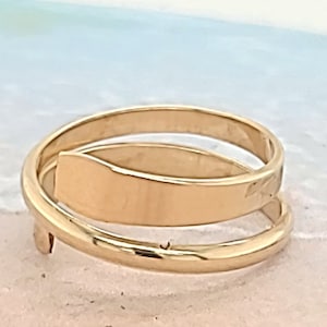 May include: A gold-toned ring with a double band design. The top band is wider and wraps around the bottom band.