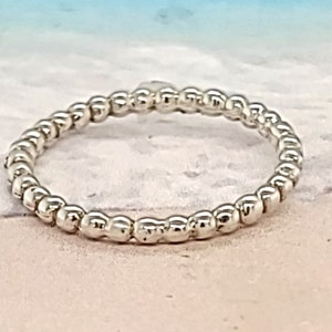 May include: A silver beaded ring on a white sandy beach background.
