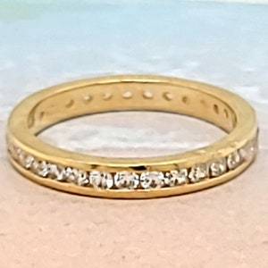May include: A thin gold band ring with a row of small clear stones set in the band.