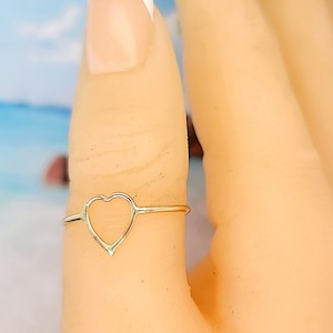 May include: A gold-toned ring with a heart-shaped design. The ring is worn on a finger.
