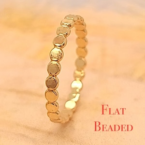May include: A gold flat beaded ring. The ring is made of small, round beads that are connected together to form a continuous band.