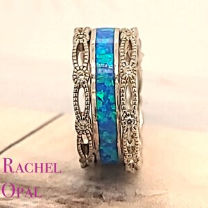 May include: A silver ring set with three bands. The center band is a blue opal, and the outer bands are silver with a delicate floral design.