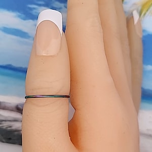 May include: A thin, iridescent ring on a finger. The ring has a rainbow of colors, including purple, green, and blue.