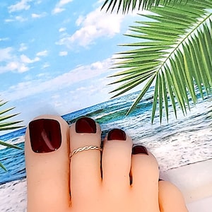 May include: A close-up of a foot with a gold toe ring. The toes are painted a dark brown color. The foot is resting on a white surface with a blue and green background.