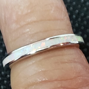 May include: A thin silver band ring with a white opal inlay.