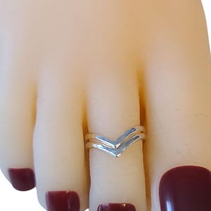 May include: A silver V-shaped toe ring. The ring is worn on a foot with polished maroon toenails. The ring has a double band design, with a textured finish. The ring is a simple, elegant accessory.