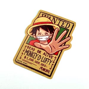May include: A sticker featuring a cartoon illustration of Monkey D. Luffy from One Piece. The design is a wanted poster with the text "WANTED" at the top, and "DEAD OR ALIVE" and "MONKEY D. LUFFY" below. The sticker is tan and has a white background.