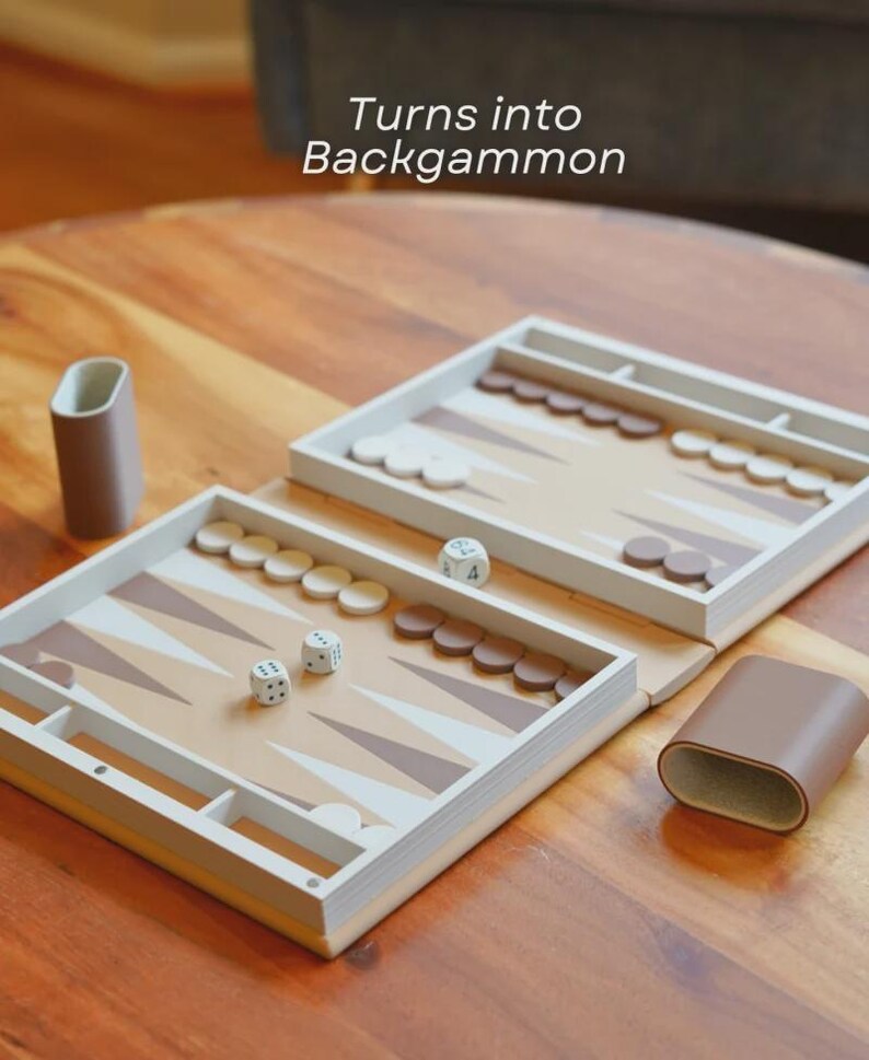 Puede incluir: Un juego de backgammon con una superficie de juego marr&oacute;n claro y blanca, dados y fichas. El texto "Turns into Backgammon" es visible. El juego est&aacute; abierto sobre una mesa de madera, con un estuche marr&oacute;n.