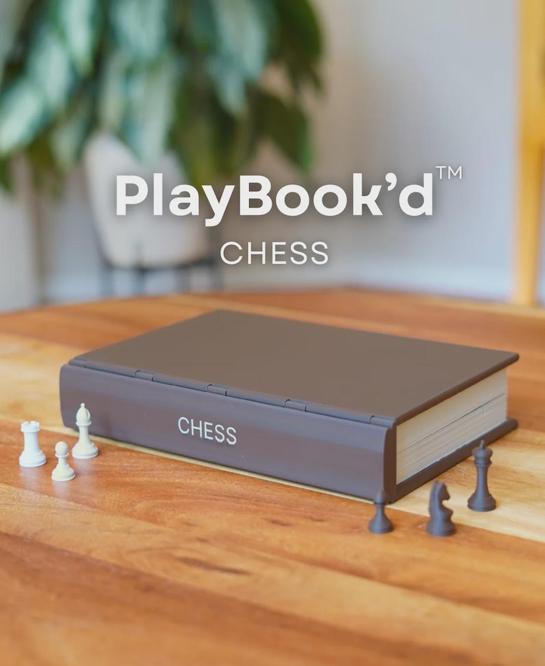 May include: A closed, brown chess set in the shape of a book, with the word "CHESS" printed on the side. White and black chess pieces are arranged on a wooden surface. The text "PlayBook'd" is at the top.