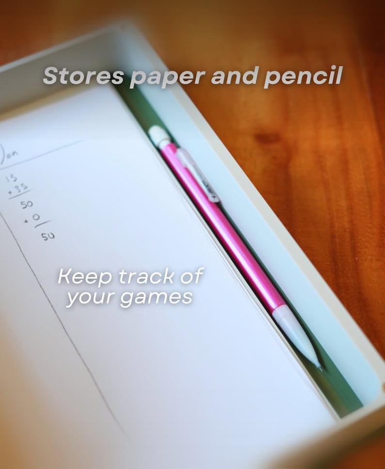 May include: A white tray with a pink pen and a notepad. The notepad has handwritten numbers and the text "Keep track of your games" and "Stores paper and pencil". The pen is pink with a white tip.