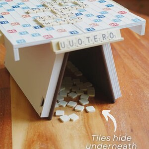 May include: A Scrabble-themed game table with a white and blue game board top. The table has a white frame with brown edges. The text "UUOTERO" is visible on the front. The text "Tiles hide underneath" is also visible.