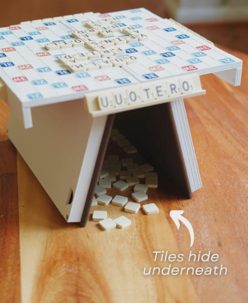 May include: A Scrabble-themed game table with a white and blue game board top. The table has a white frame with brown edges. The text "UUOTERO" is visible on the front. The text "Tiles hide underneath" is also visible.