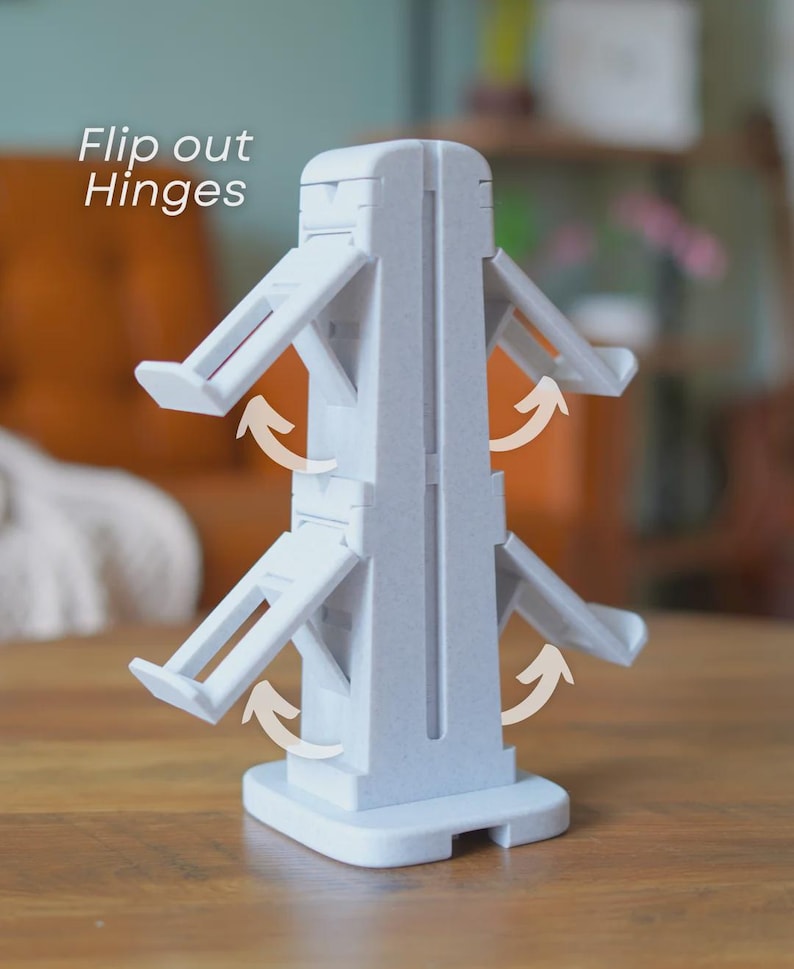 Może przedstawiać: Jasnoszare plastikowe urządzenie z odchylanymi zawiasami, przeznaczone do stania w pozycji pionowej na płaskiej powierzchni. Tekst "Flip out Hinges" jest widoczny w lewym g&oacute;rnym rogu. Zawiasy są pokazane w pozycji otwartej z zakrzywionymi strzałkami.