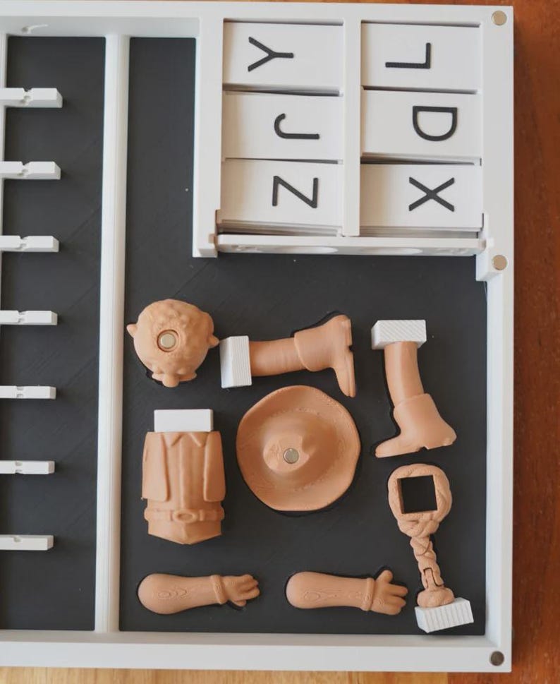 May include: A white framed puzzle with a black interior. The puzzle contains a set of white letter tiles and several tan-coloured puzzle pieces, including a head, arms, legs, a hat, and a jacket. The puzzle pieces are arranged in a specific order.