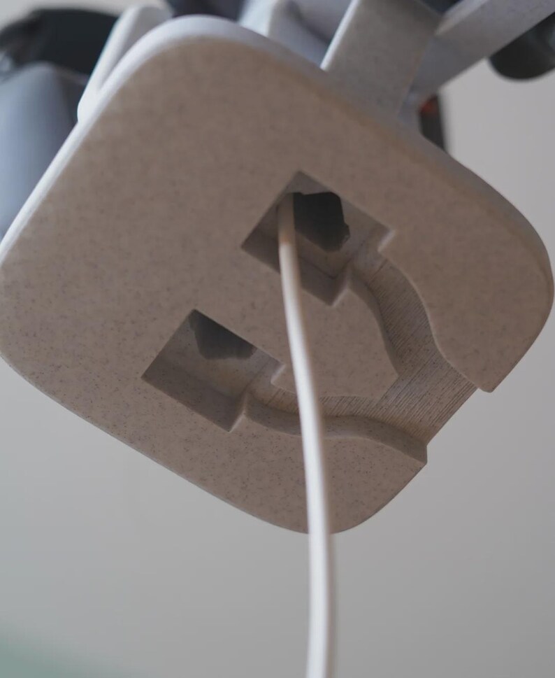 Może przedstawiać: Zbliżenie jasnobeżowego, teksturowanego, kwadratowego obiektu z białym przewodem wychodzącym z kwadratowego otworu. Obiekt ma rzeźbiony wz&oacute;r i jest umieszczony na miękkim, neutralnym tle.