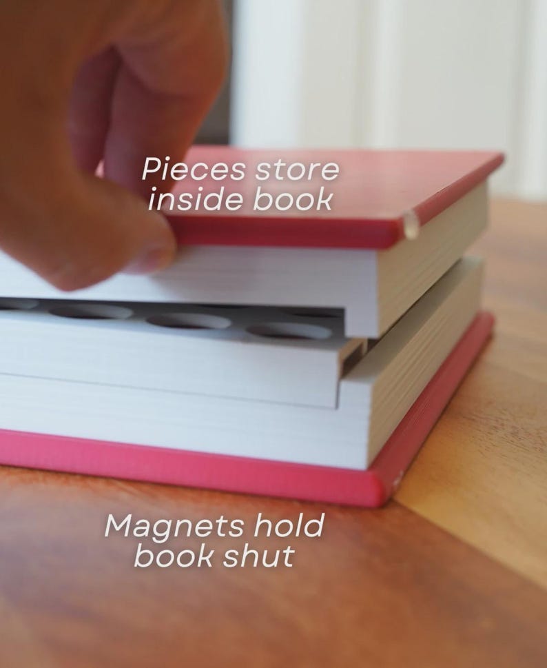 Może przedstawiać: Czerwono-biała książka z tekstem "Pieces store inside book" i "Magnets hold book shut". Książka jest otwarta, odsłaniając schowek. Książka leży na drewnianej powierzchni.