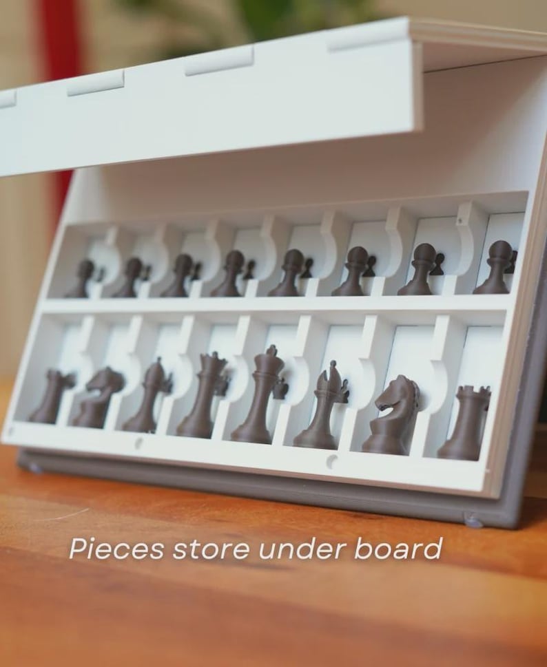 May include: A white and gray chess set with brown chess pieces. The pieces are stored in a compartment under the board. The text "Pieces store under board" is visible on the bottom of the image.