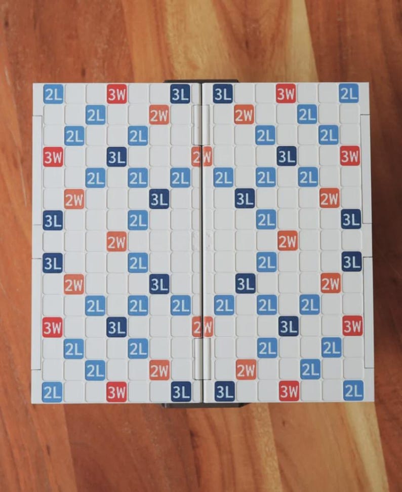 May include: A Scrabble board game, folded open, featuring a grid of white squares with blue, red, and orange text. The board is set on a wooden surface. The game board is designed for word-building.