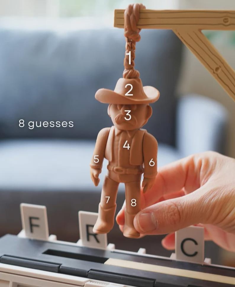 May include: A tan cowboy figurine suspended from a wooden gallows, part of a game. The figurine wears a hat, shirt, and boots. The text "8 guesses" is visible. The letters F, R, and C are also present.