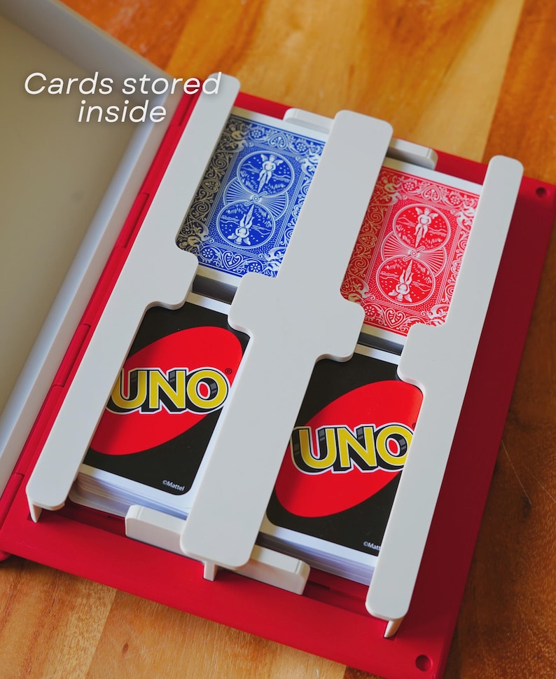 May include: A red card holder with white dividers, holding decks of UNO and playing cards. The text "Cards stored inside" is visible. The UNO cards are red and yellow. The playing cards have blue and red backs.