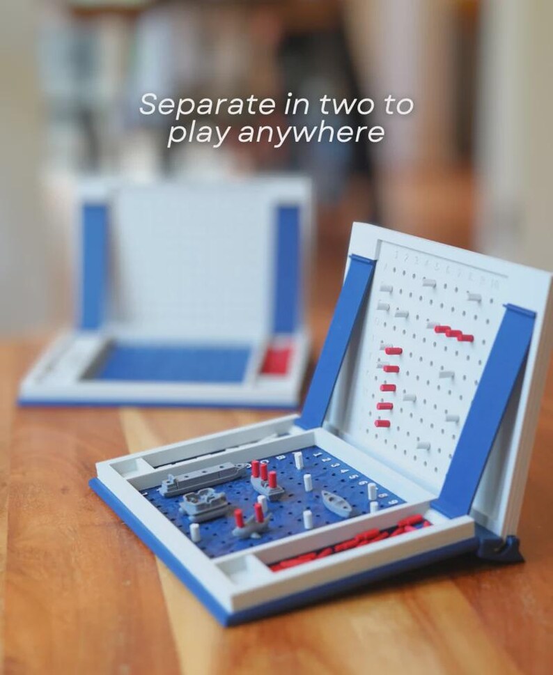 Op de afbeelding: Een klassiek Zeeslag-spel in een blauw en witte behuizing. Het spelbord is open en onthult een blauw raster met miniatuurschepen en pinnen. De tekst "Separate in two to play anywhere" is zichtbaar.