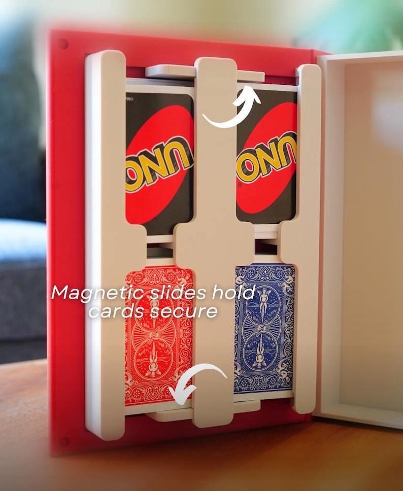 May include: A red and white card holder with two decks of cards. One deck is an UNO card, and the other is a blue and red deck of cards. The text "Magnetic slides hold cards secure" is visible.