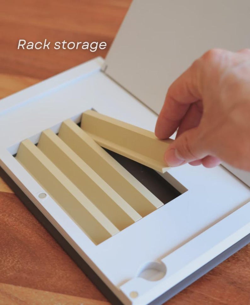 May include: A white and beige rack storage unit with a hand placing a beige divider. The unit has a rectangular frame with multiple beige dividers. The text "Rack storage" is visible in the upper left corner.