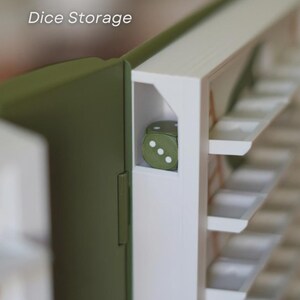 May include: A close-up of a dice storage box. The box is olive green and white, with the text "Dice Storage" in the upper left corner. A single green die with white dots is visible inside the box. The box has multiple shelves.