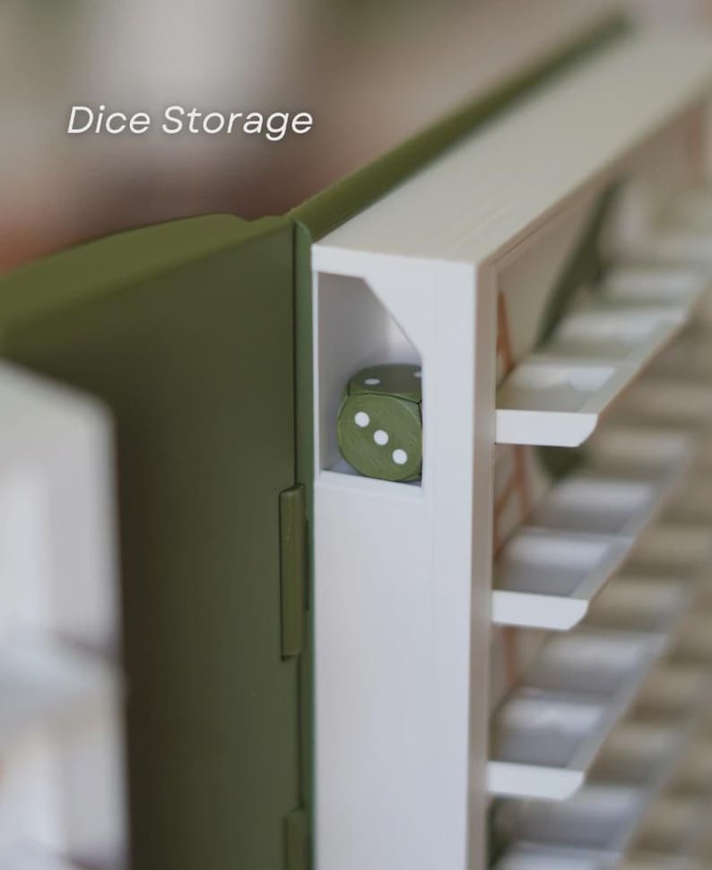 May include: A close-up of a dice storage box. The box is olive green and white, with the text "Dice Storage" in the upper left corner. A single green die with white dots is visible inside the box. The box has multiple shelves.