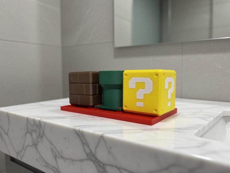 May include: A set of three decorative items: a brown brick block, a green pipe, and a yellow question mark block. The items are arranged on a red base, reminiscent of a video game theme. The question mark block has white question marks on two sides.
