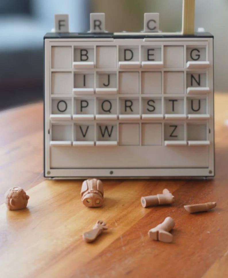 May include: A vintage word game with a white and black frame, featuring letter tiles and small, brown game pieces scattered on a wooden surface. The letters visible are B, D, E, G, I, J, N, O, P, Q, R, S, T, U, V, W, and Z.