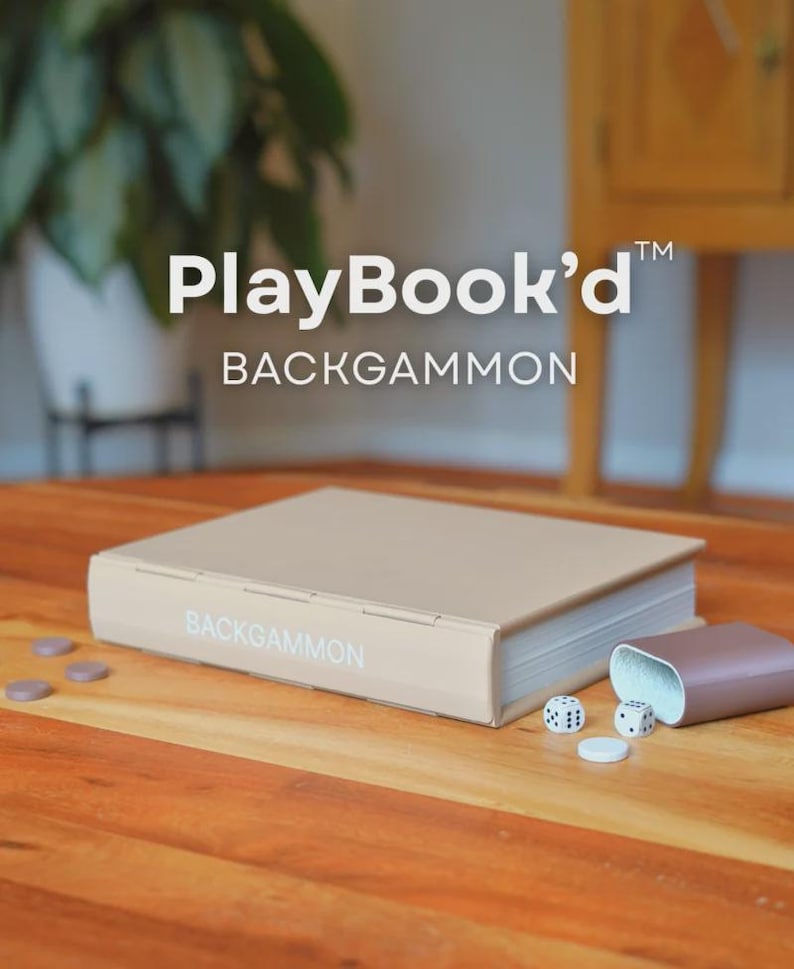 Puede incluir: Un juego de Backgammon beige con el texto "PlayBook'd BACKGAMMON" en la portada. El juego incluye dados, fichas y un recipiente marr&oacute;n. El juego se muestra sobre una superficie de madera.