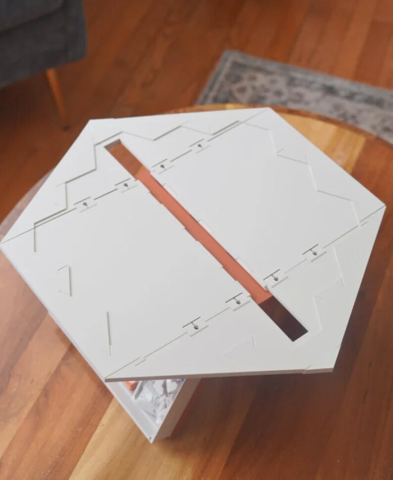 May include: A white, geometric puzzle with a central, rectangular, brown-colored channel. The puzzle is composed of multiple pieces and has a complex, angular design. The object is placed on a wooden surface.