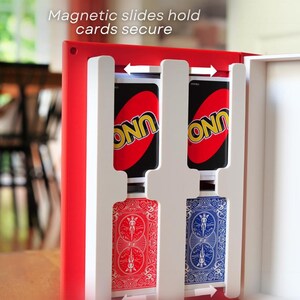 May include: A red card holder with white dividers, holding two Uno cards and two Bicycle playing cards. The text "Magnetic slides hold cards secure" is visible. The holder is designed to keep cards organized.