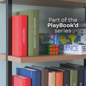 May include: A shelf displays a collection of board games from the PlayBook'd series. Games include Checkers, Snakes and Ladders, and others. The games are in colorful boxes, with the text "Part of the PlayBook'd series" visible.