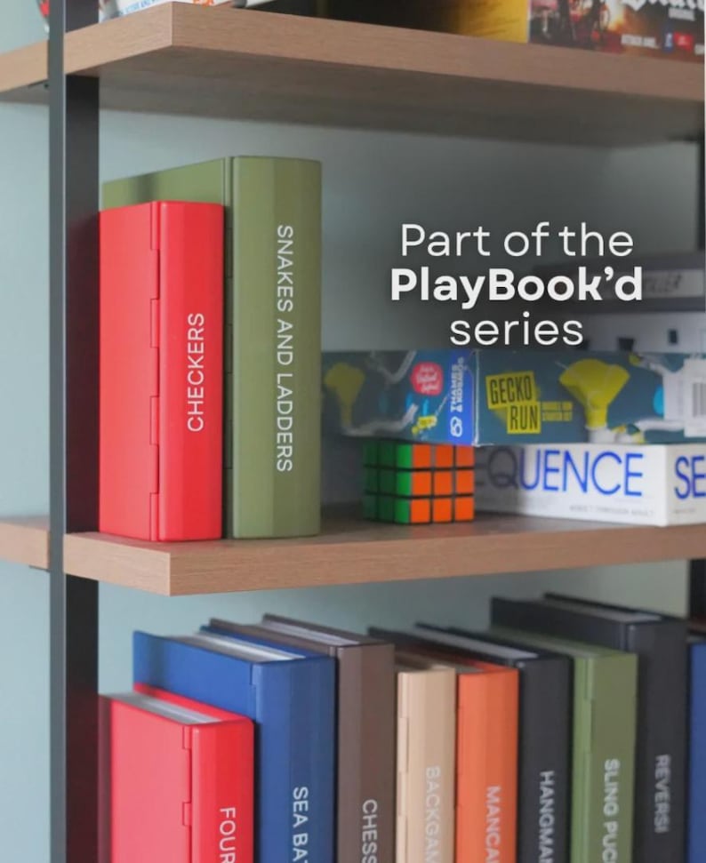 May include: A shelf displays a collection of board games from the PlayBook'd series. Games include Checkers, Snakes and Ladders, and others. The games are in colorful boxes, with the text "Part of the PlayBook'd series" visible.