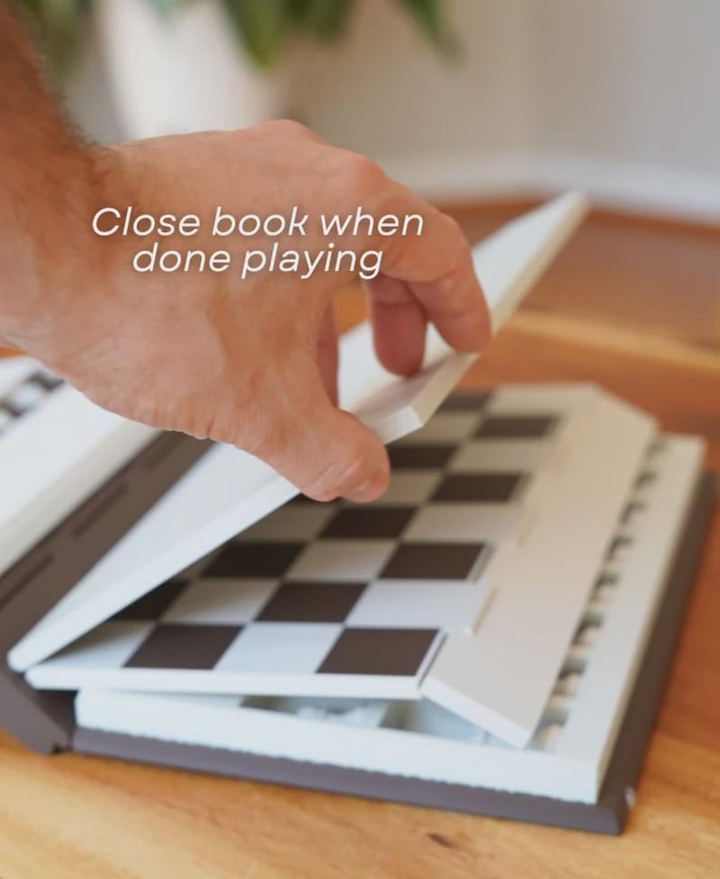 May include: A portable chess set with a brown and white exterior. The chess board is black and white. The text "Close book when done playing" is visible on the top of the image.