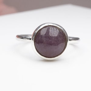 以下が含まれることがあります： ベゼルセッティングにセットされた丸い紫色の宝石が付いたシルバーリングです。