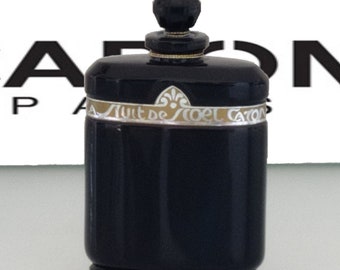 Op de afbeelding: Een zwarte glazen fles Caron's Nuit de Noel parfum met een gouden en zilveren label waarop "Nuit de Noel Caron" staat.