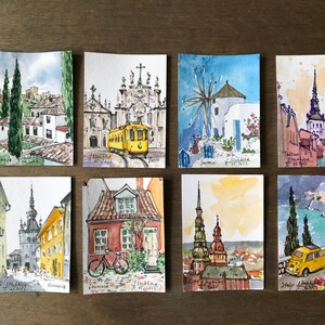 May include: A collection of eight watercolor paintings depicting various European cities. Each painting features a unique architectural element, such as a church, windmill, or tower, and is painted in a realistic style with vibrant colors.