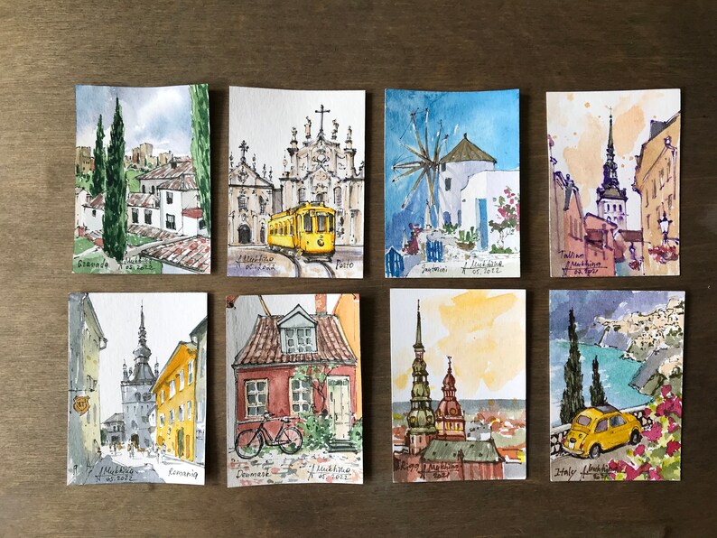 May include: A collection of eight watercolor paintings depicting various European cities. Each painting features a unique architectural element, such as a church, windmill, or tower, and is painted in a realistic style with vibrant colors.