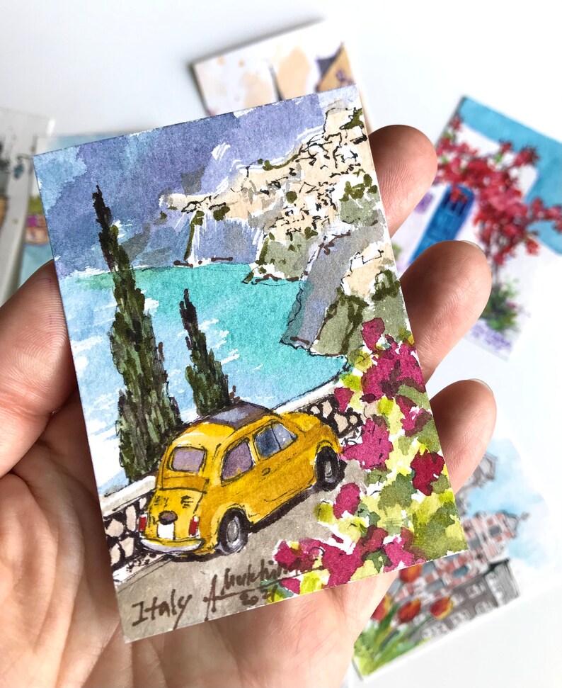 May include: A watercolor painting of a yellow Fiat car driving along a winding road with a view of a blue ocean and a rocky cliffside. The painting is signed "Italy" and dated "2021".