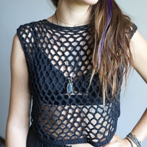 May include: A black crochet top with a black and silver pendant necklace. The top is a fishnet style and the pendant is a dark blue stone.
