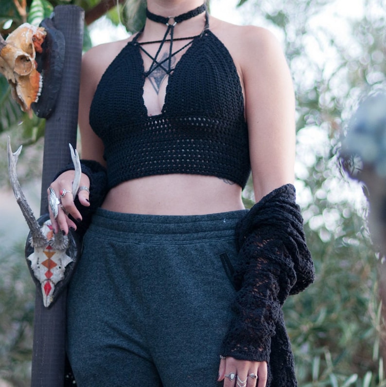Peut inclure: Un haut de bikini noir en crochet avec un motif d'&eacute;toile et un collier ras du cou noir. Le haut est port&eacute; avec un pantalon de surv&ecirc;tement gris fonc&eacute; et un cardigan noir en crochet.