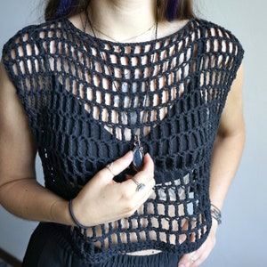 May include: A black crochet top with a large, dark gemstone pendant necklace. The top is sleeveless and has a loose, flowing fit.