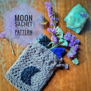 Op de afbeelding: Een grijze gehaakte tas met een zwart halve maan ontwerp. De tas is gevuld met verschillende kristallen, waaronder blauwe, paarse en groene. De tekst "MOON SACHET CROCHET PATTERN" is geschreven in een paarse zeshoek.