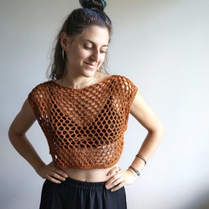 May include: A brown crochet top with a loose, open-weave design. The top has a scoop neckline and sleeveless design.