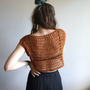 May include: A brown crochet top with a loose, open-weave design. The top is sleeveless and cropped, with a scoop neckline.
